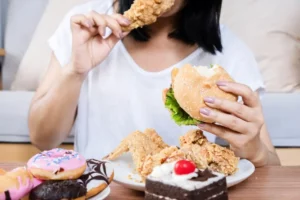 Binge eating disorder concept with woman eating fast food burger, fried chicken, donuts and desserts 