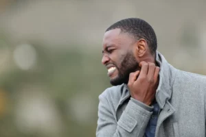 Stressed man with black skin scratching itchy neck in winter in a park. 