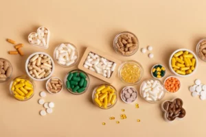 Many different coloured vitamins, food supplements and minerals in glass jars, ceramic small plate and wooden box on a beige background top view. Vitamin d, c, e, b, a, k, magnesium, zinc, probiotics. 