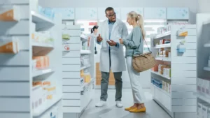 Pharmacy: Professional Black Pharmacist Helping Caucasian Senior Female Customer with Medicine Recommendation, Advice, Talking. Customer Support in Drugstore Full of Drugs, Pills, Health Care Products. 