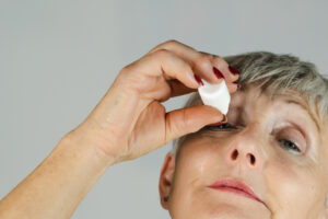 Older woman looking up applying eye drops on white background