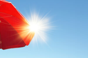 Parasol with sun rays. Red beach umbrella sheltering the strong summer sun in the blue sky.