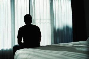 A depressed man sitting on a bed in a darkened room