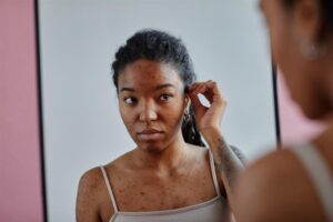 Portrait of young black woman with acne scars looking in mirror insecure in appearance. 