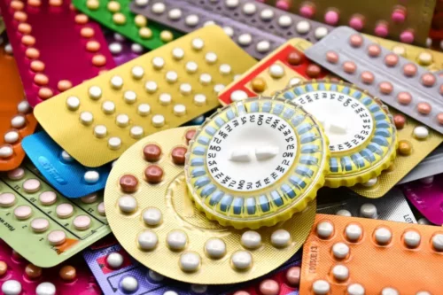 Oral contraceptive pill on pharmacy counter with colourful pills strips background.