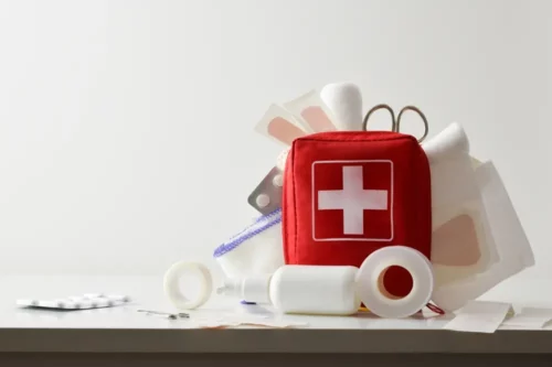 Travel portable first aid bag full of objects and tools for minor cures on white table. Front view. Horizontal composition.