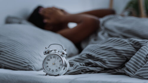 African woman suffering from insomnia lying in bed without sleep with alarm clocks close-up, panorama.