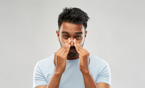 health problem and people concept - Indian man rubbing nose over grey background.