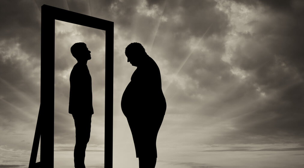 obese man looking at a reflection of a younger man in a mirror