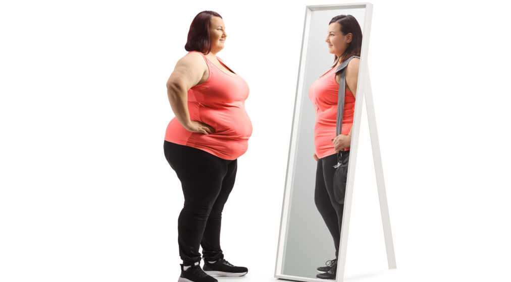 Overweight woman looking at a slimmer version of herself in the mirror isolated on white background