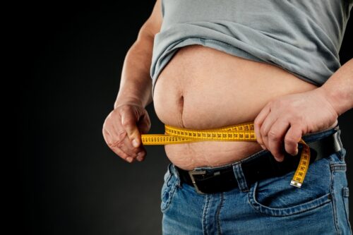 A man measures his fat belly with a measuring tape. on a black background.