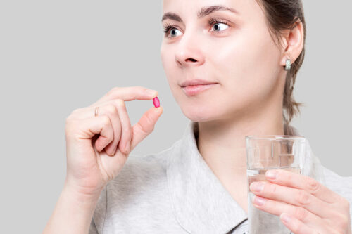 young woman is holding red vitamin tablet and glass of water. Concept of health. The girl takes pill. Care for health. Treatment with medication. Prevention of diseases