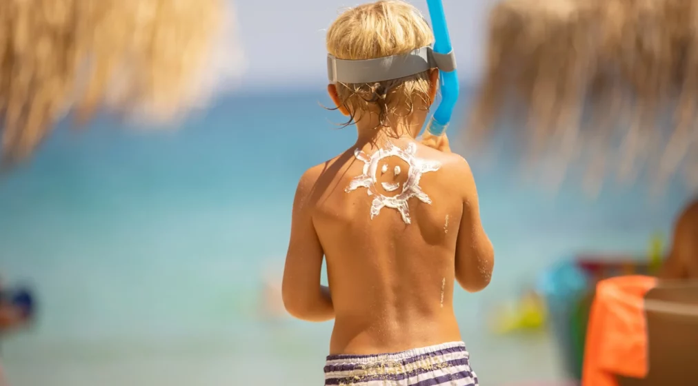 Happy child, blond boy on the beach with applied sunscreen, enjoying summer, playing.