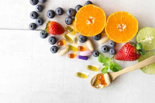 Multivitamins and supplements with fresh and healthy fruits on white wooden background.