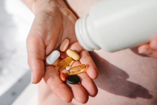 Closeup photo of supplements with a white bottle. Pregnant woman takes omega 3, multivitamins, vitamins B, C, D, collagen tablets, probiotics, iron capsule. Girl holds vitamins daily. Top view.